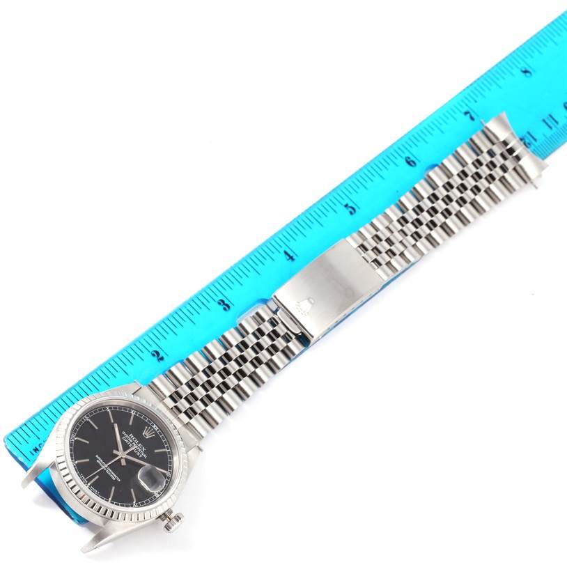 The Rolex Datejust 16220 Men
s Stainless Steel Black Dial 16220 Men
s Stainless Steel Black Dial watch is shown from a top-down angle, displaying the entire watch including the face, crown, and bracelet next to a ruler.