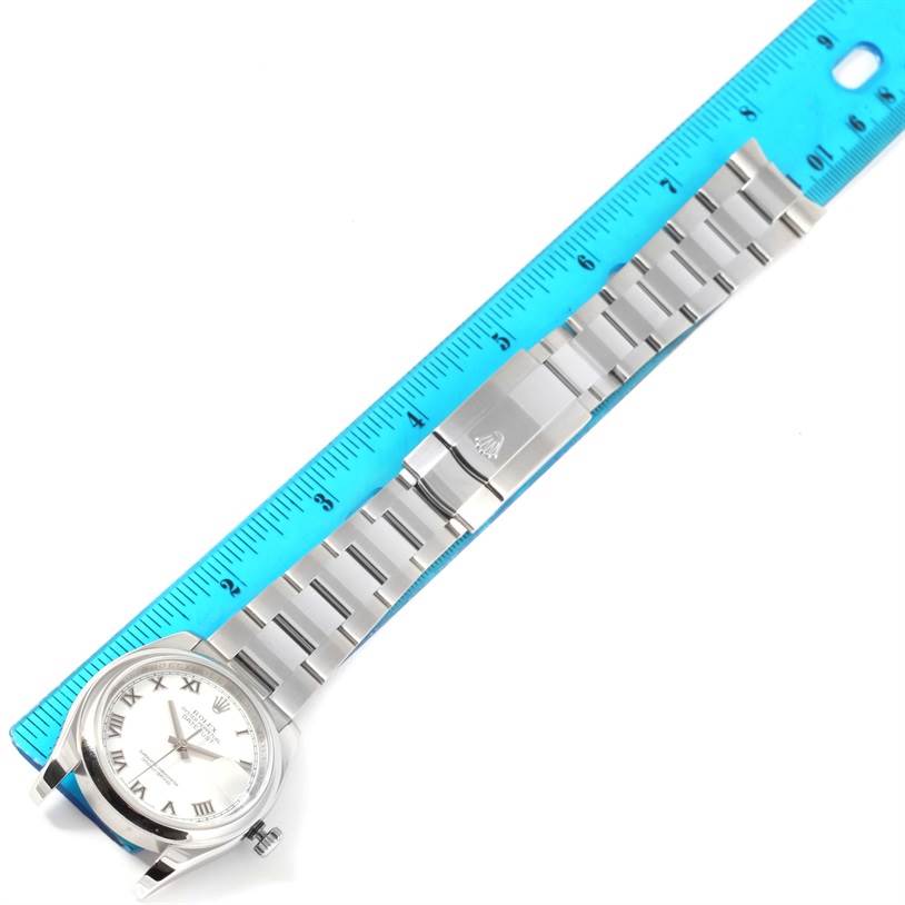 The image shows a Rolex Datejust 116200 Men
s Stainless Steel White Dial 116200 Men
s Stainless Steel White Dial watch laid flat alongside a ruler, showcasing its dial and stainless steel bracelet.