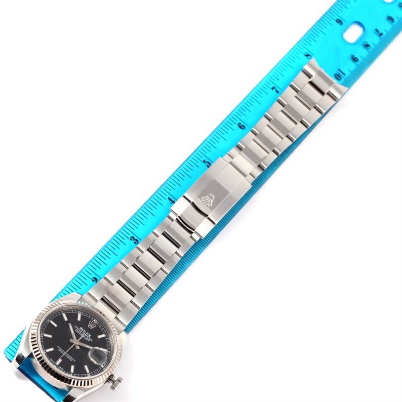 This image shows a top-down view of a Rolex Datejust 116234 Men
s Stainless Steel Black Dial 116234 Men
s Stainless Steel Black Dial watch, focusing on the face and metal bracelet, placed next to a blue ruler.