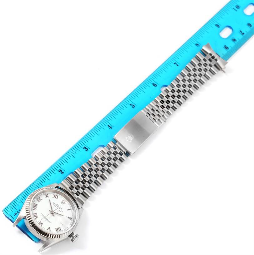 The image shows a Rolex Datejust 16234 Men
s Stainless Steel White Dial 16234 Men
s Stainless Steel White Dial watch from above, with its face, bracelet, and clasp placed alongside a blue ruler.