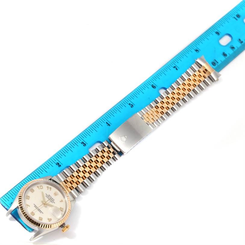 The image shows a top-down view of a Rolex Datejust 16233 Men
s Steel and Gold (two tone) Beige Dial 16233 Men
s Steel and Gold (two tone) Beige Dial watch, revealing its face, bezel, and Jubilee bracelet with a clasp, alongside a ruler.