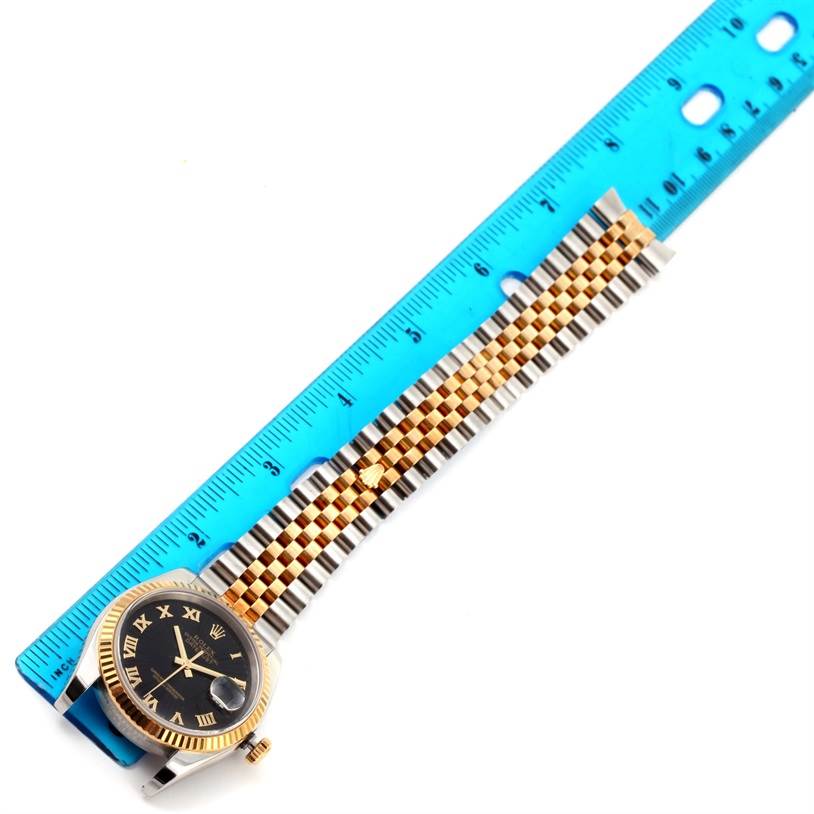 The Rolex Datejust 116233 Men
s Stainless Steel Black Dial 116233 Men
s Stainless Steel Black Dial watch is shown from a top-down angle, displaying the face, bezel, and part of the bracelet alongside a ruler.