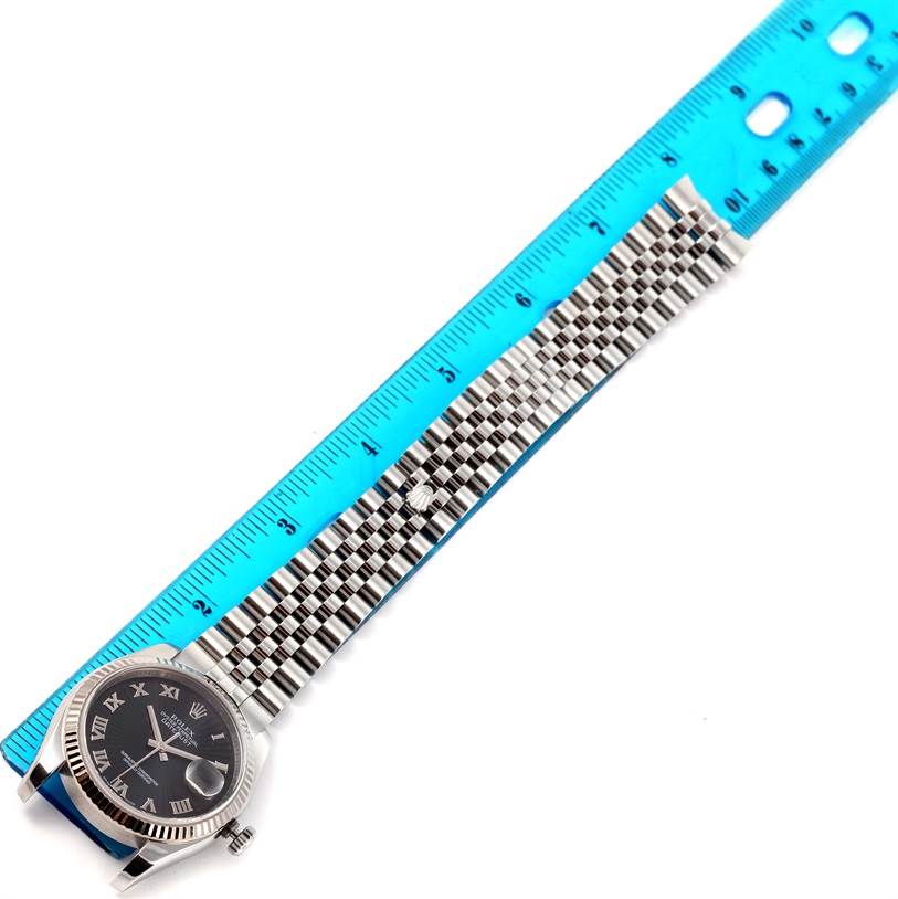The image shows a top view of a Rolex Datejust 116234 Men
s Stainless Steel Black Dial 116234 Men
s Stainless Steel Black Dial watch, focusing on its face and metal bracelet next to a blue ruler.
