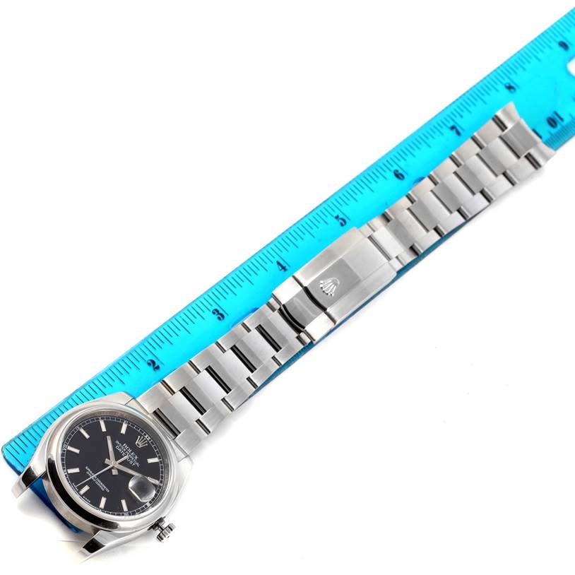 The image shows a Rolex Datejust 116200 Men
s Stainless Steel Black Dial 116200 Men
s Stainless Steel Black Dial watch laid flat with a blue ruler alongside it for measurement.