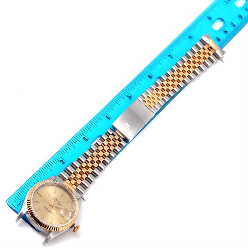 The image shows a Rolex Datejust 16233 Men's Steel and Gold (two tone) Champagne Dial 16233 Men's Steel and Gold (two tone) Champagne Dial watch laid flat alongside a blue ruler, displaying the face, bracelet, and clasp.