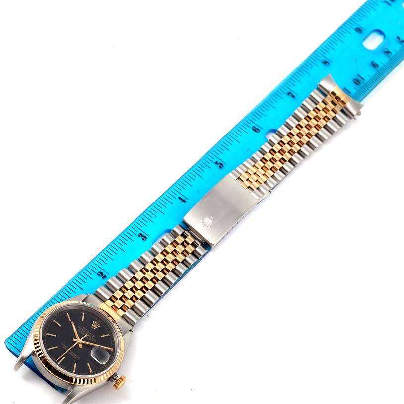 This image shows a Rolex Datejust 16233 Men's Steel and Gold (two tone) Black Dial 16233 Men's Steel and Gold (two tone) Black Dial watch viewed from above, positioned next to a blue ruler for scale.