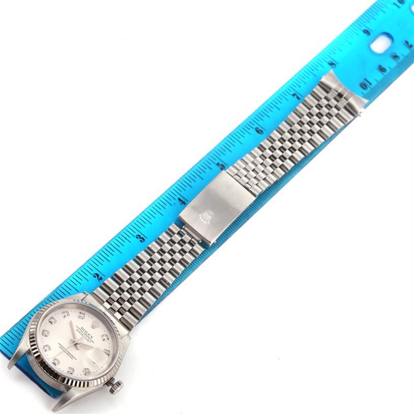 The Rolex Datejust 16234 Men's Stainless Steel Silver Dial 16234 Men's Stainless Steel Silver Dial watch is shown from a top-down angle, displaying the face, bracelet, and clasp next to a blue ruler. 