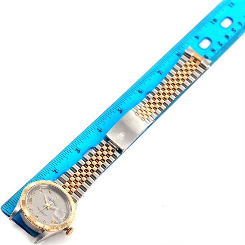 The image shows a Rolex Datejust 16263 Men's Steel and Gold (two tone) Grey Dial 16263 Men's Steel and Gold (two tone) Grey Dial watch laying flat next to a blue ruler, highlighting its full length and bracelet with clasp.