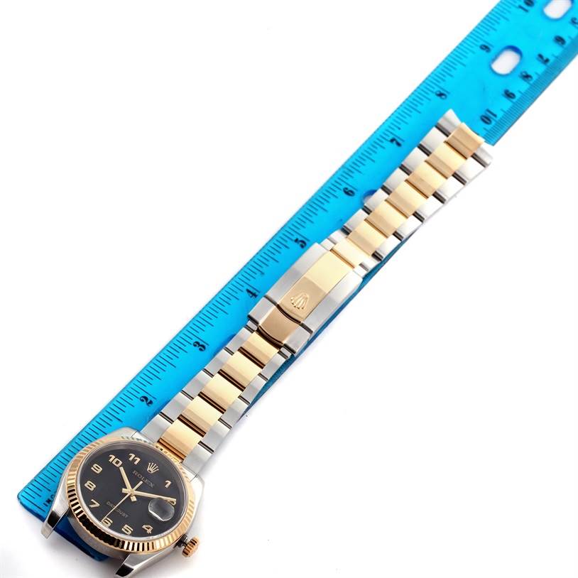 The Rolex Datejust 116233 Men
s Stainless Steel Black Dial 116233 Men
s Stainless Steel Black Dial watch is shown horizontally with the face, bracelet, and clasp visible, next to a blue ruler.