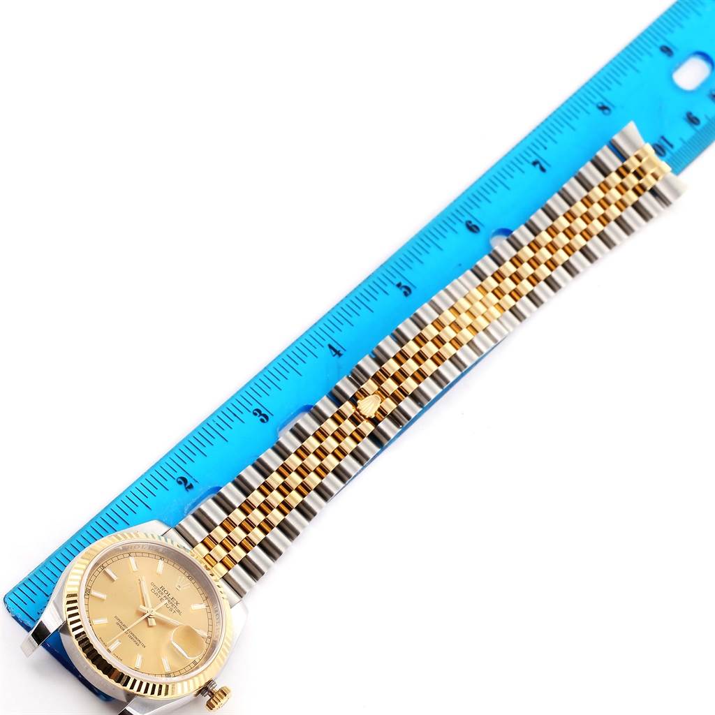 The image shows a Rolex Datejust 116233 Men's Stainless Steel Champagne Dial 116233 Men's Stainless Steel Champagne Dial watch at a top-down angle, featuring a gold dial and a two-tone bracelet next to a ruler.