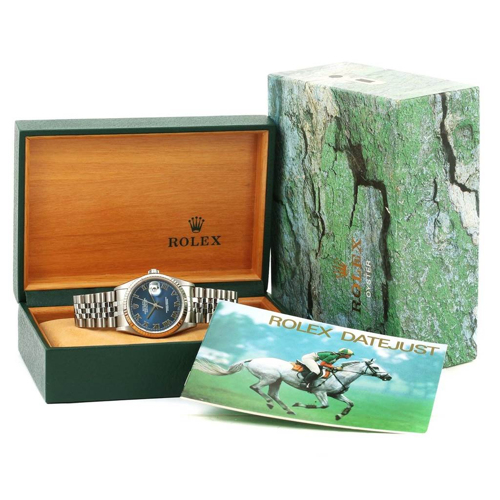 The Rolex Datejust 16234 Men's Stainless Steel Blue Dial 16234 Men's Stainless Steel Blue Dial watch is shown from a front angle, with its packaging and a booklet in the background.