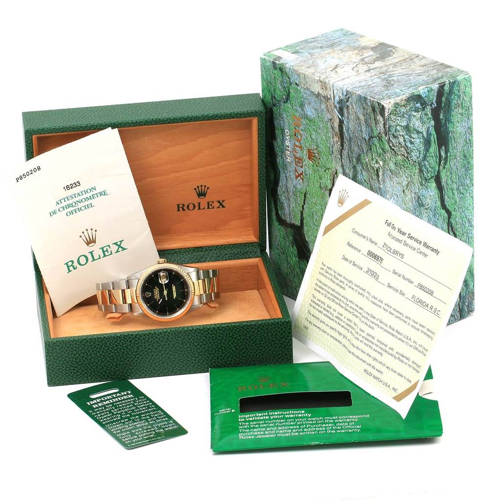 The Rolex Datejust 16233 Men's Steel and Gold (two tone) Black Dial 16233 Men's Steel and Gold (two tone) Black Dial watch and accessories are shown at an oblique angle, including its box and documentation.