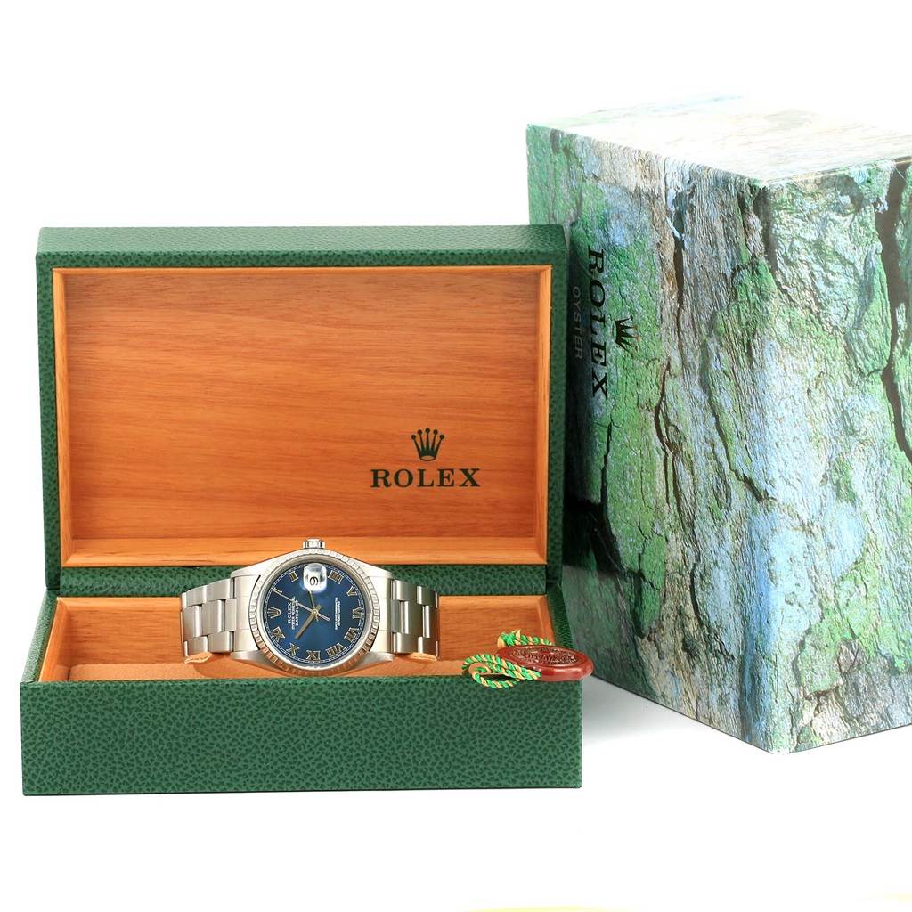 The Rolex Datejust 16220 Men's Stainless Steel Blue Dial 16220 Men's Stainless Steel Blue Dial watch is displayed front-facing inside its open green and wooden box, with the outer packaging visible beside it.
