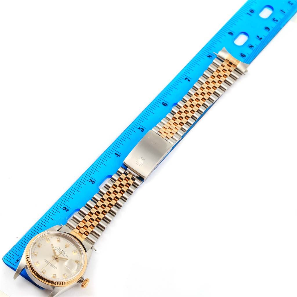 This image shows a Rolex Datejust 16233 Men
s Steel and Gold (two tone) Silver Dial 16233 Men
s Steel and Gold (two tone) Silver Dial watch laid flat with its band next to a blue ruler.