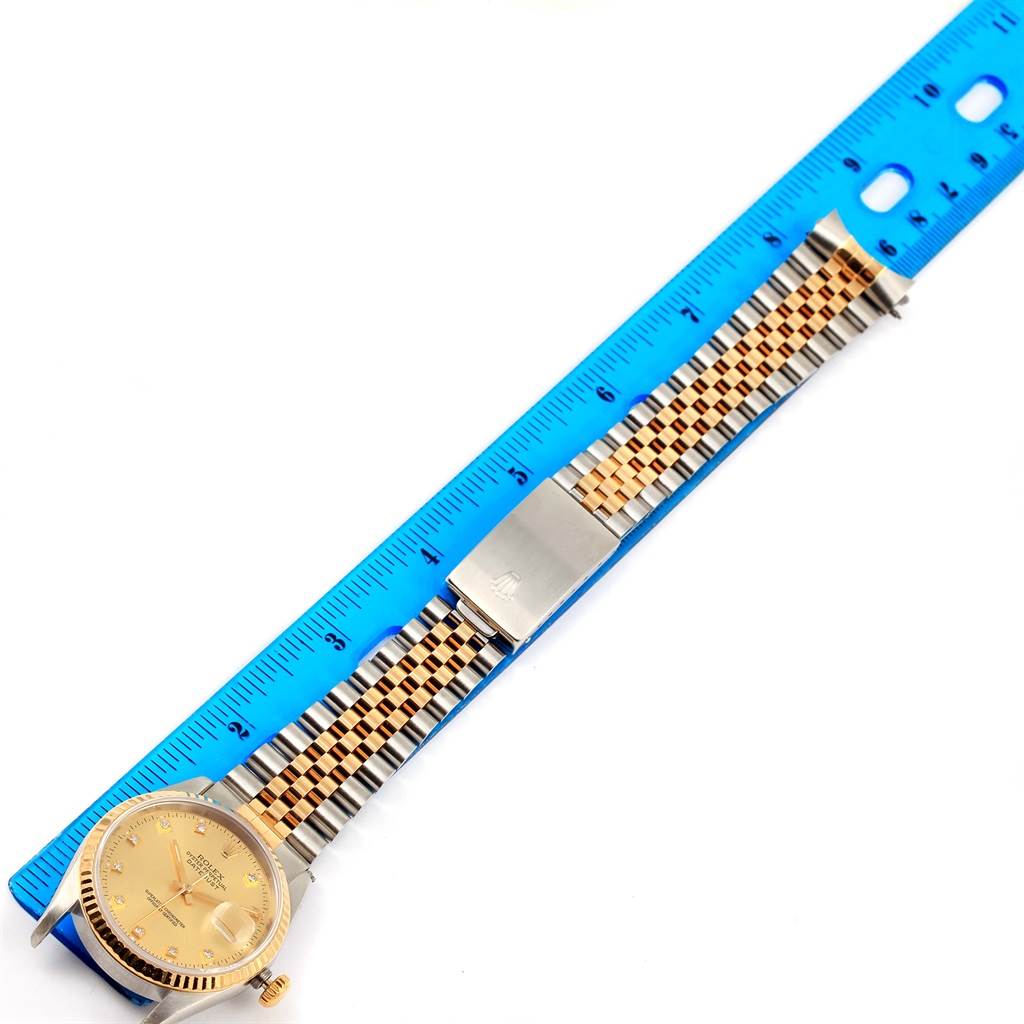 The Rolex Datejust 16233 Men
s Steel and Gold (two tone) Champagne Dial 16233 Men
s Steel and Gold (two tone) Champagne Dial watch is pictured from above with a focus on its dial, two-tone bracelet, and clasp next to a blue ruler.