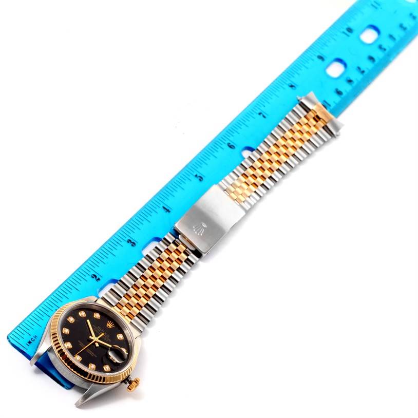 This image shows a Rolex Datejust 16233 Men's Steel and Gold (two tone) Black Dial 16233 Men's Steel and Gold (two tone) Black Dial watch, featuring a two-tone bracelet and black dial, placed next to a blue ruler.