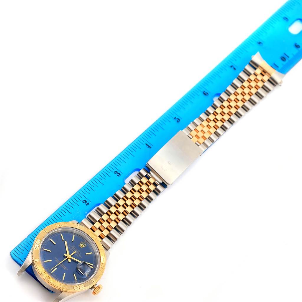 The image shows a Rolex Datejust 16263 Men's Steel and Gold (two tone) Blue Dial 16263 Men's Steel and Gold (two tone) Blue Dial watch with a blue face and two-tone metal bracelet, alongside a blue ruler.