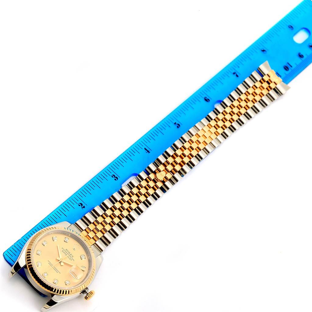 The Rolex Datejust 116233 Men
s Stainless Steel Champagne Dial 116233 Men
s Stainless Steel Champagne Dial watch is shown from a top-down angle, displaying its face, crown, and bracelet alongside a blue ruler.