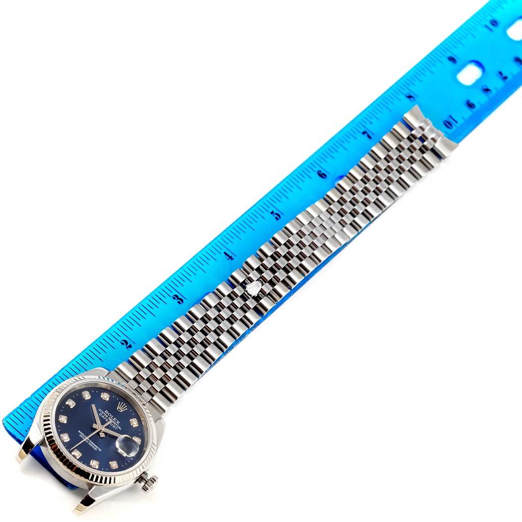 The image shows a top-down view of a Rolex Datejust 116234 Men's Stainless Steel Blue Dial 116234 Men's Stainless Steel Blue Dial watch with a blue face and linked bracelet beside a blue ruler for scale.