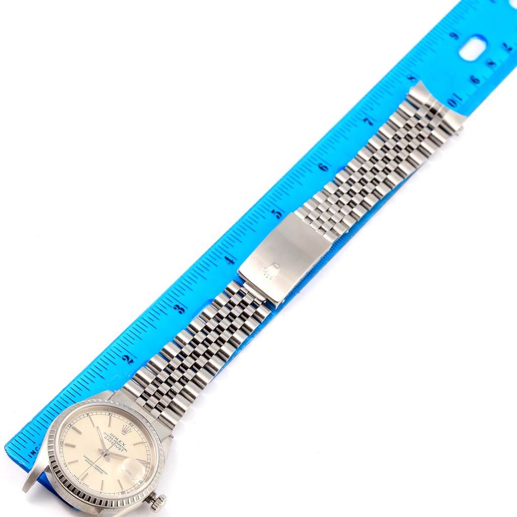 The Rolex Datejust 16220 Men
s Stainless Steel Silver Dial 16220 Men
s Stainless Steel Silver Dial watch is shown from a top-down angle, highlighting the face, bezel, and metal bracelet with a ruler for scale.