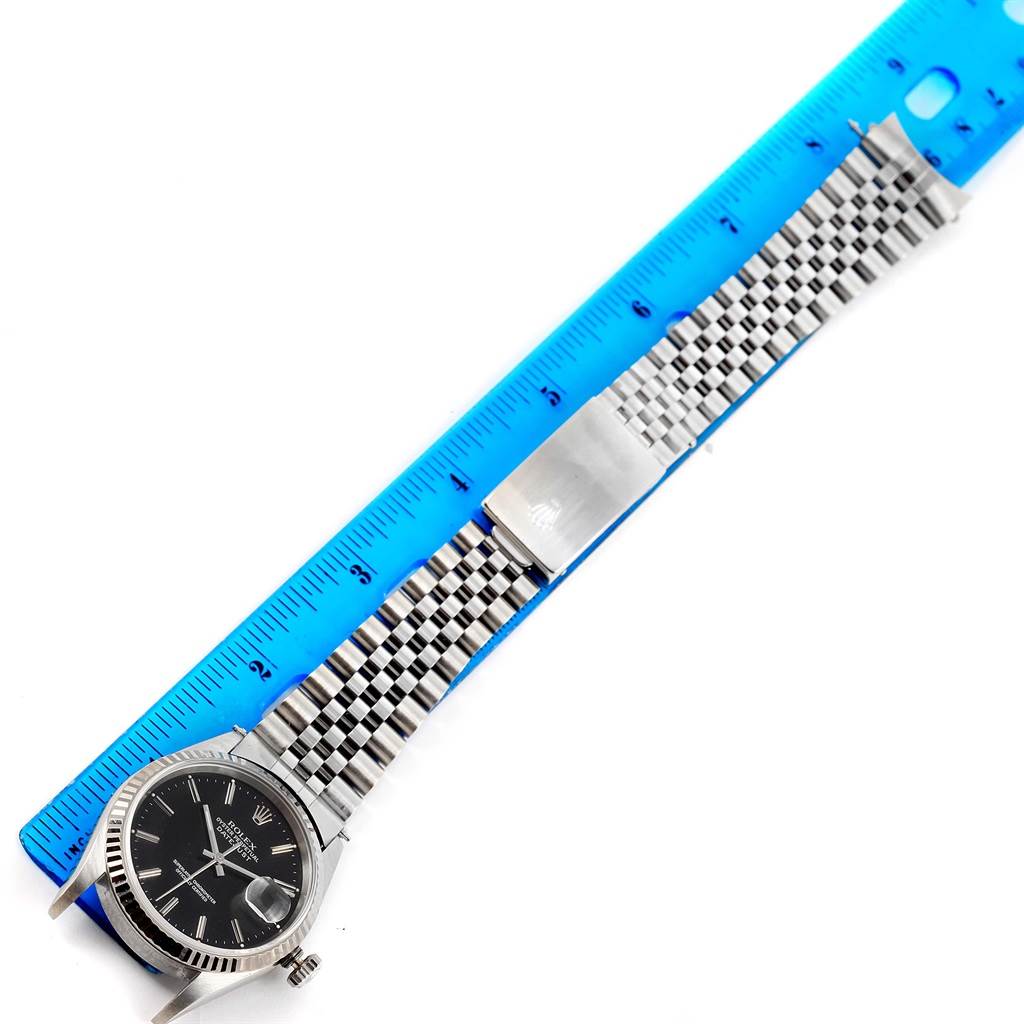 The Rolex Datejust 16234 Men
s Stainless Steel Silver Dial 16234 Men
s Stainless Steel Silver Dial watch is shown from a top-down angle, displaying the face, bezel, and stainless steel bracelet extended alongside a blue ruler.