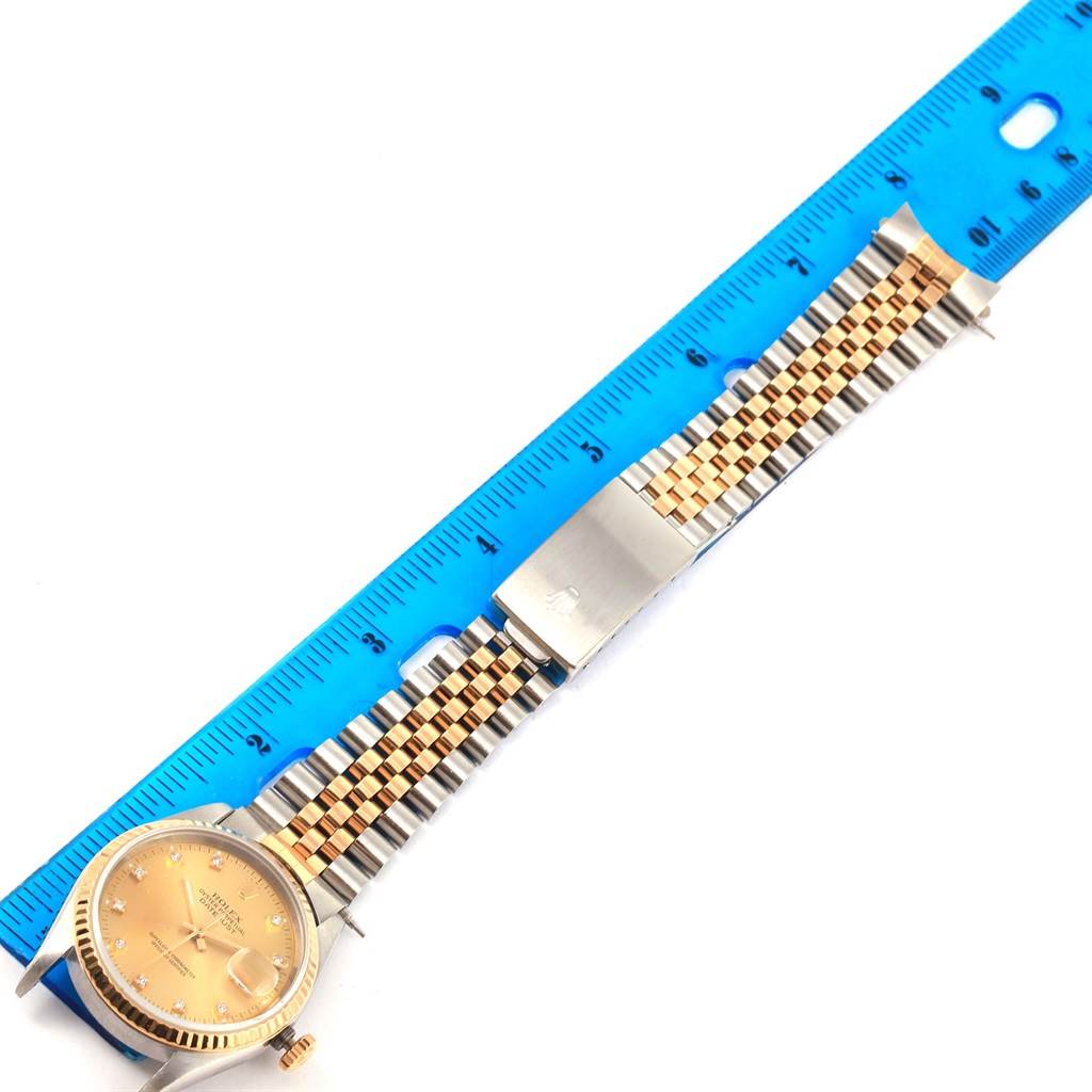 The Datejust model by Rolex is shown from a top-down angle with the full watch face and the metal strap aligned with a blue ruler.