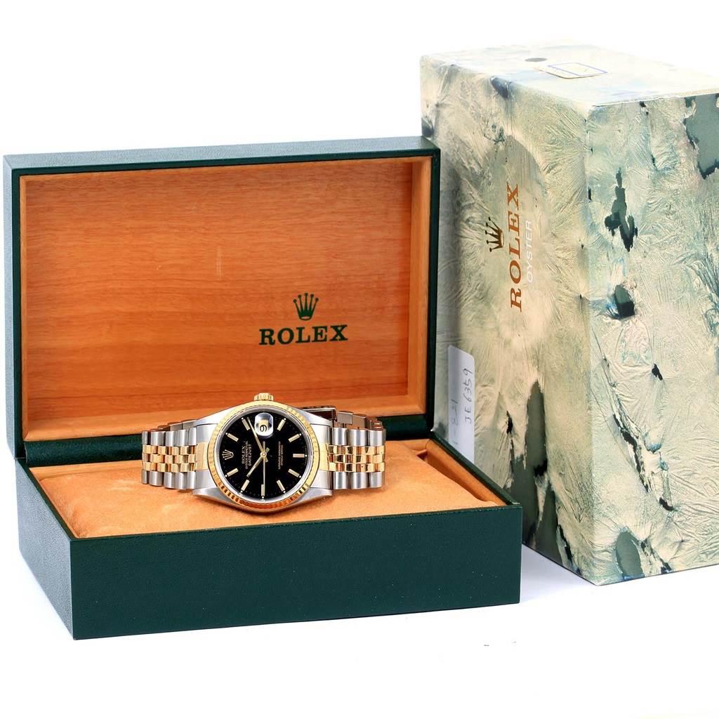The image shows a Rolex Datejust 16233 Men
s Steel and Gold (two tone) Black Dial 16233 Men
s Steel and Gold (two tone) Black Dial watch with a black dial, placed in an open green and wooden display box, along with its outer packaging.