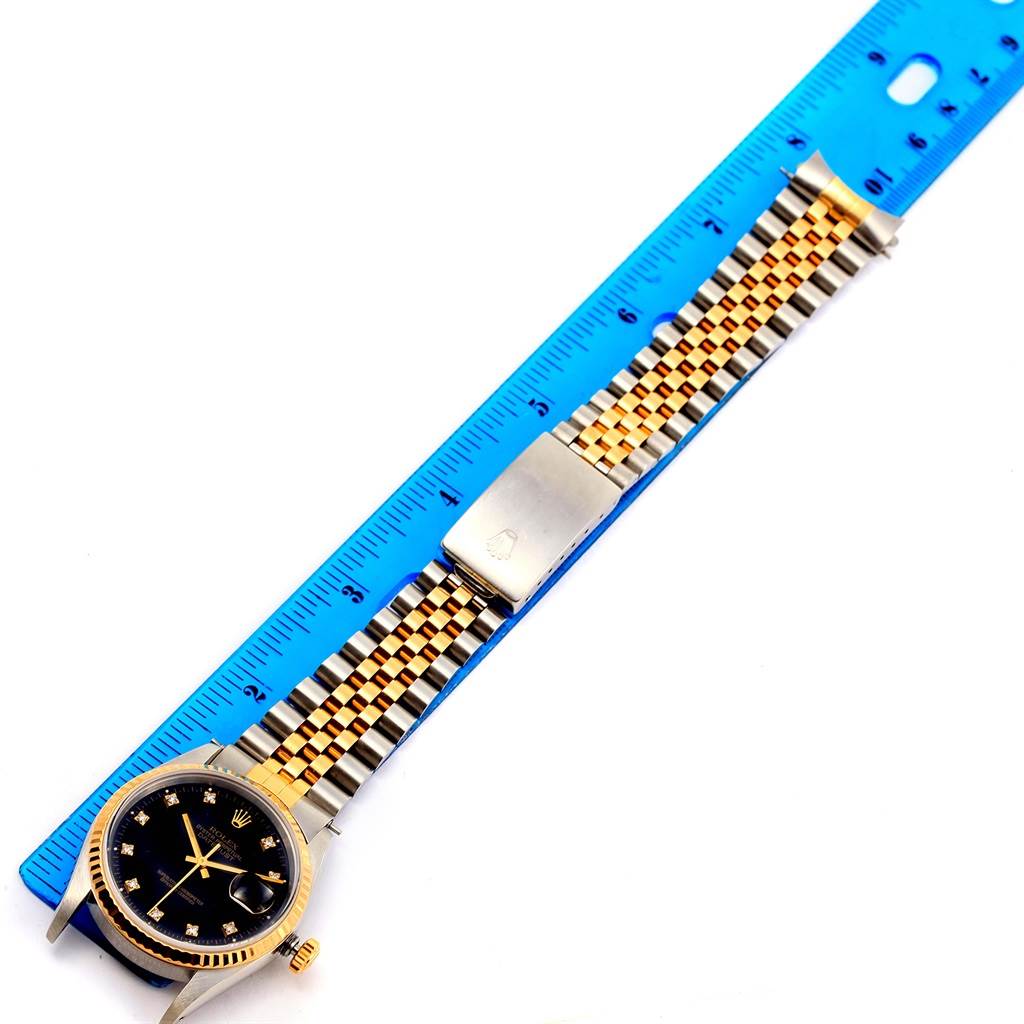 The image shows the Rolex Datejust 16233 Men's Steel and Gold (two tone) Black Dial 16233 Men's Steel and Gold (two tone) Black Dial watch lying flat, with the face, bezel, bracelet, and folding clasp visible alongside a ruler.