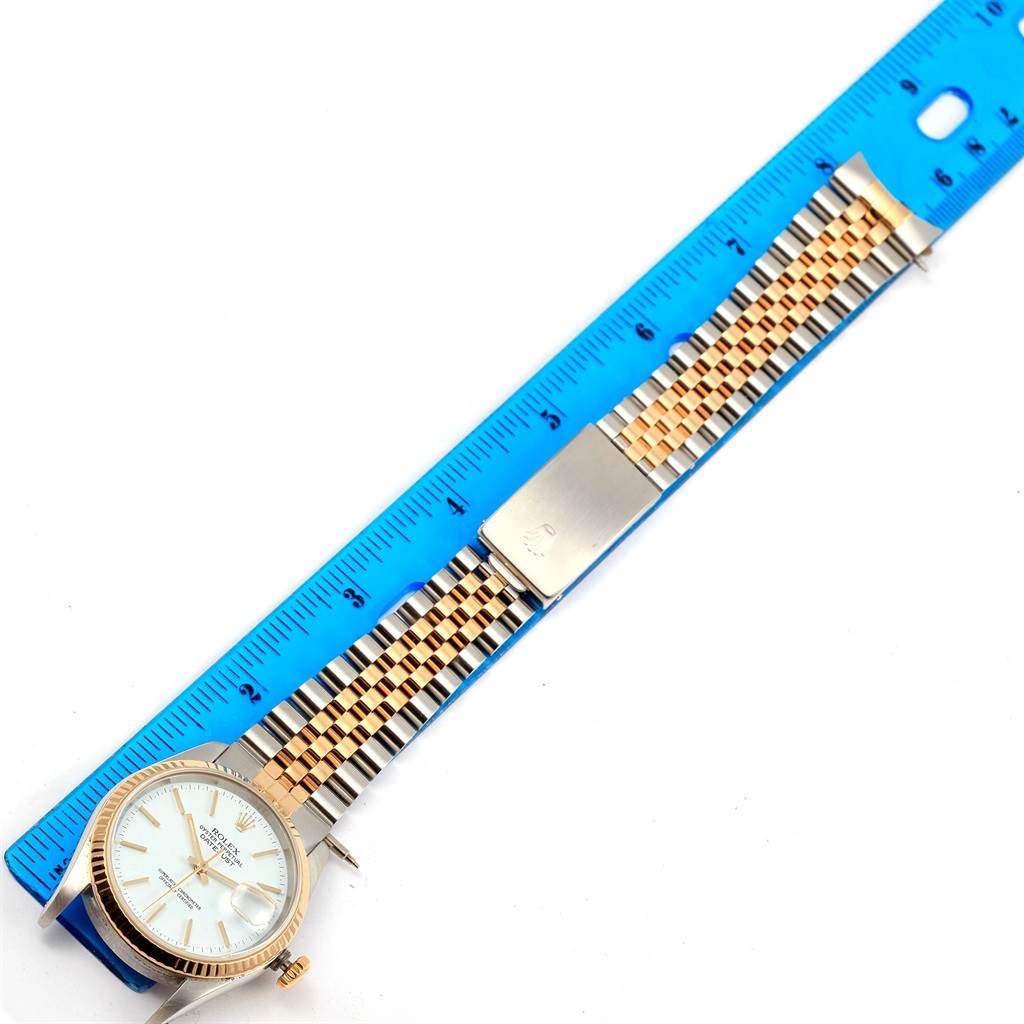 The image shows a Rolex Datejust 16233 Men's Steel and Gold (two tone) White Dial 16233 Men's Steel and Gold (two tone) White Dial watch lying flat, highlighting its face, jubilee bracelet, and deployment clasp next to a blue ruler.