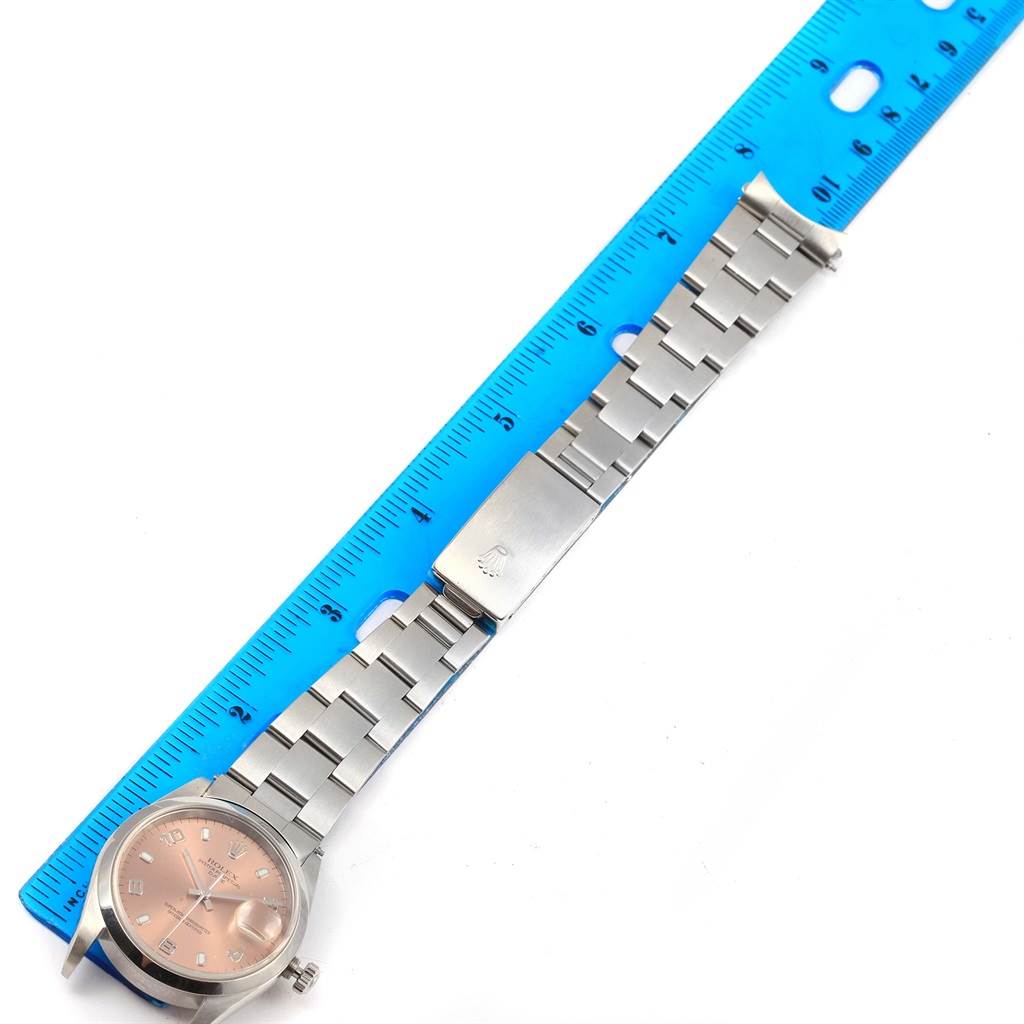 The image shows a Rolex Datejust 15200 Men's Stainless Steel Pink Dial 15200 Men's Stainless Steel Pink Dial watch face-up with its bracelet extended beside a blue ruler for measurement.