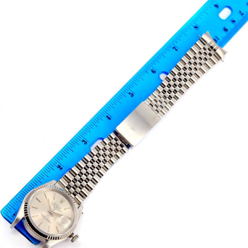 The Rolex Datejust 16234 Men's Stainless Steel Silver Dial 16234 Men's Stainless Steel Silver Dial watch is shown from an overhead angle with its face, bracelet, and clasp next to a blue ruler.