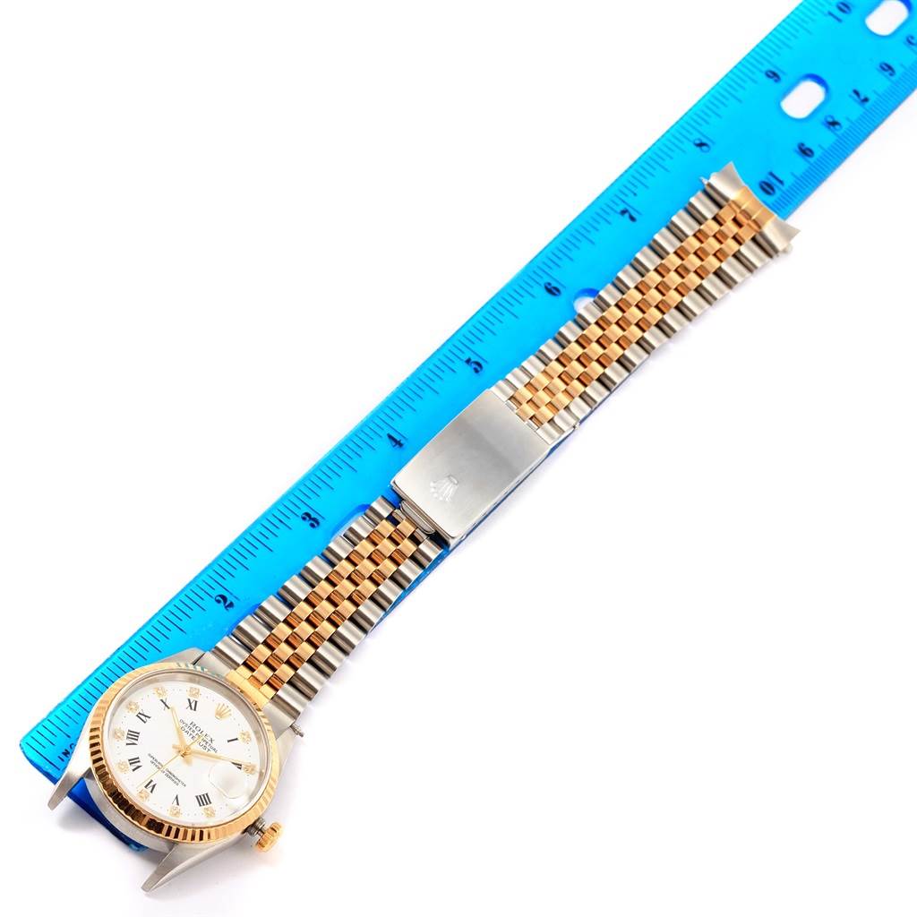The image shows a Rolex Datejust 16233 Steel and Gold (two tone) White Dial 16233 Steel and Gold (two tone) White Dial watch and its bracelet next to a blue ruler from an overhead angle.
