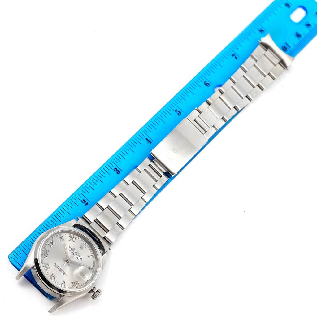 The Rolex Datejust 16200 Men's Stainless Steel Silver Dial 16200 Men's Stainless Steel Silver Dial watch is shown from a top-down angle with its band and clasp laid beside a blue ruler for scale.