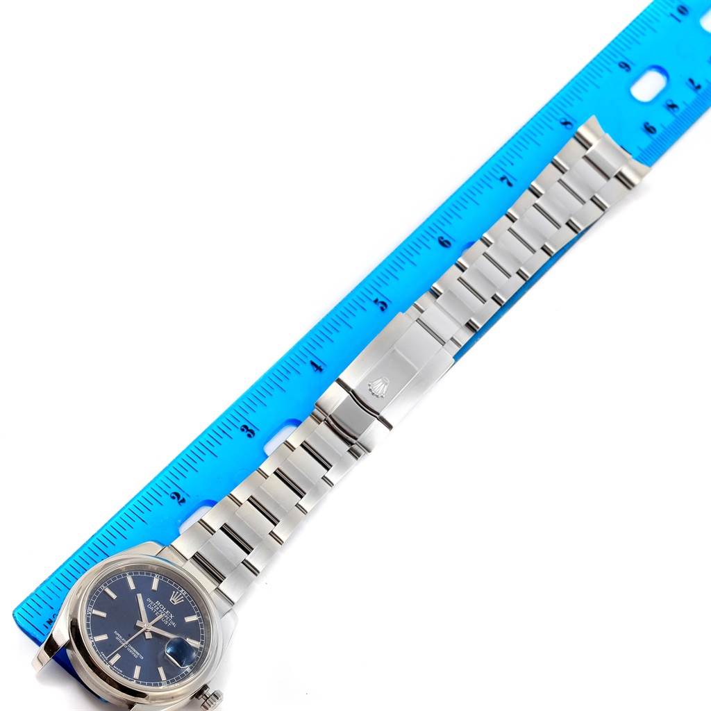 The Rolex Datejust 116200 Men's Stainless Steel Blue Dial 116200 Men's Stainless Steel Blue Dial watch is shown horizontally with its bracelet and clasp, alongside a blue ruler for measurement.