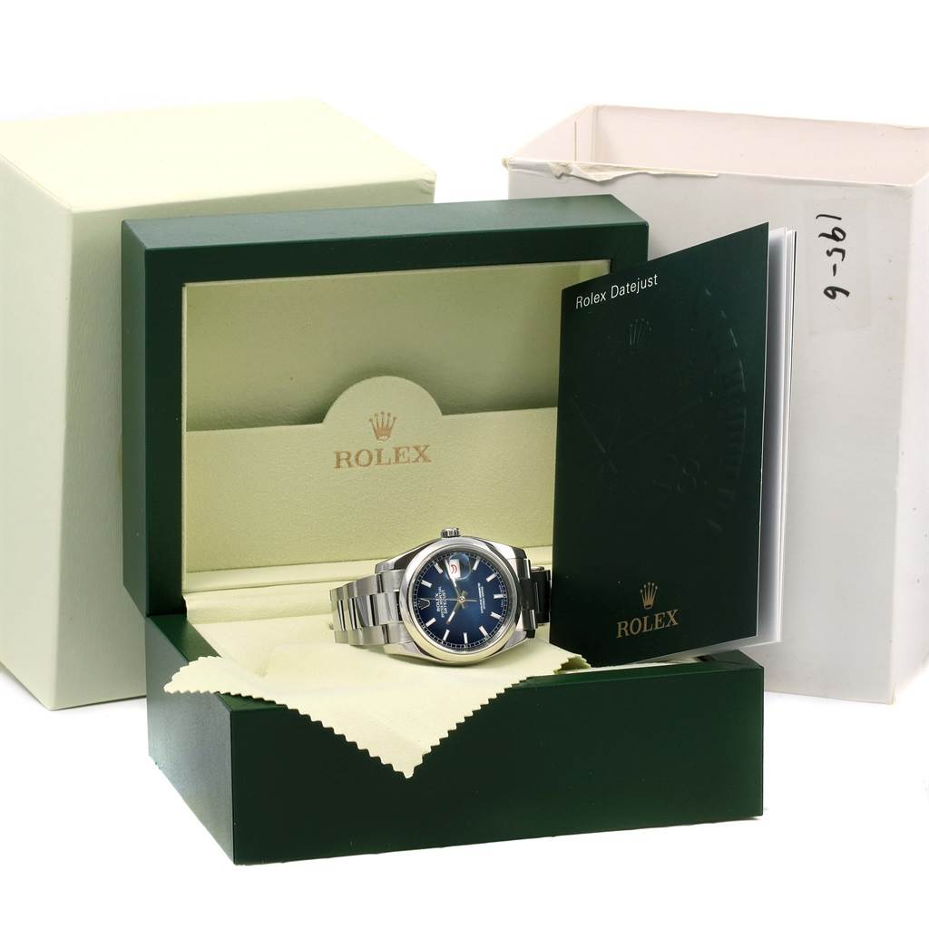 The Rolex Datejust 116200 Men's Stainless Steel Blue Dial 116200 Men's Stainless Steel Blue Dial watch is shown in an open box, with a booklet and cleaning cloth beside it.