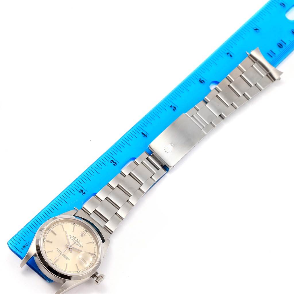 The image shows a top-down view of a Rolex Datejust 16200 Men's Stainless Steel Silver Dial 16200 Men's Stainless Steel Silver Dial watch with a stainless steel bracelet, alongside a blue ruler for scale.