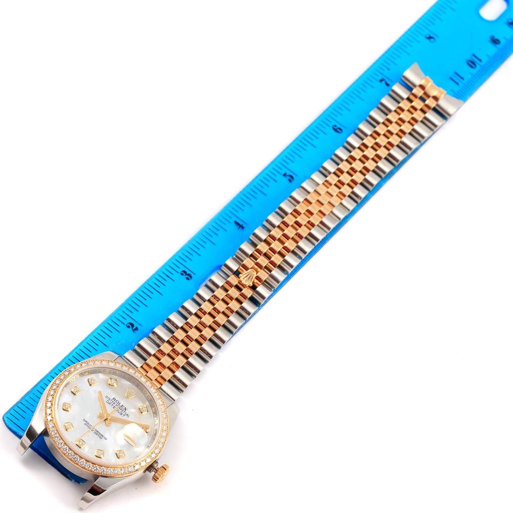 The Rolex Datejust 116243 Women's Stainless Steel Mother of Pearl Dial 116243 Women's Stainless Steel Mother of Pearl Dial watch is shown at an angle with its face, band, and part of a blue measuring ruler visible.