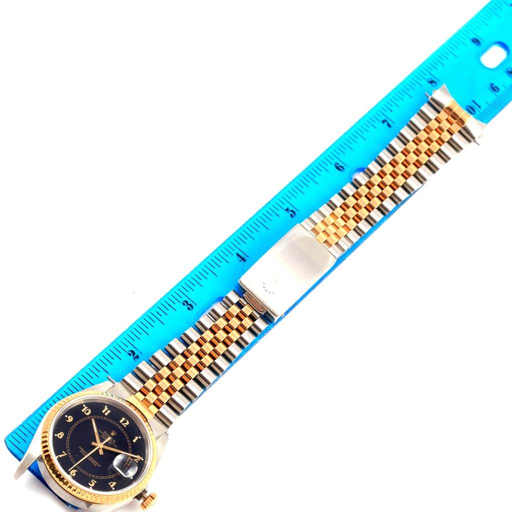 The Rolex Datejust 16233 Men's Steel and Gold (two tone) Black Dial 16233 Men's Steel and Gold (two tone) Black Dial watch is shown from a top-down angle, featuring its face, bezel, and full metal bracelet with a measuring ruler beside it.