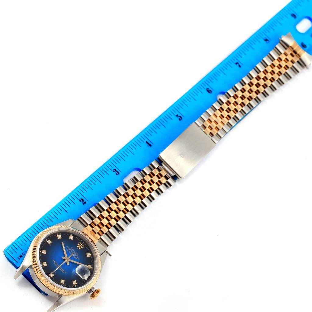 The Rolex Datejust 16233 Men's Steel and Gold (two tone) Blue Dial 16233 Men's Steel and Gold (two tone) Blue Dial watch is shown from a top-down angle, displaying its face, crown, and Jubilee bracelet next to a blue ruler.
