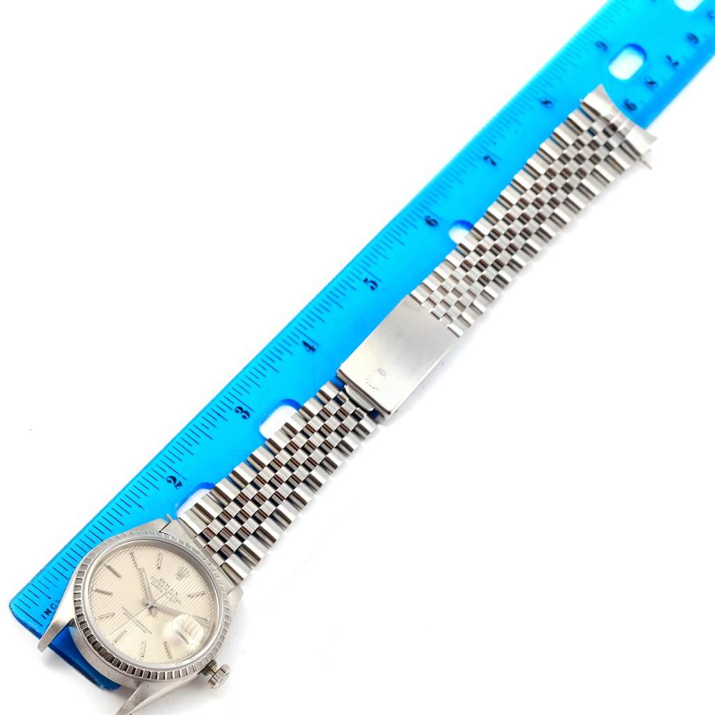 The Rolex Datejust 16220 Men's Stainless Steel Silver Dial 16220 Men's Stainless Steel Silver Dial watch is shown lying flat next to a ruler, displaying its face, bracelet, and clasp.