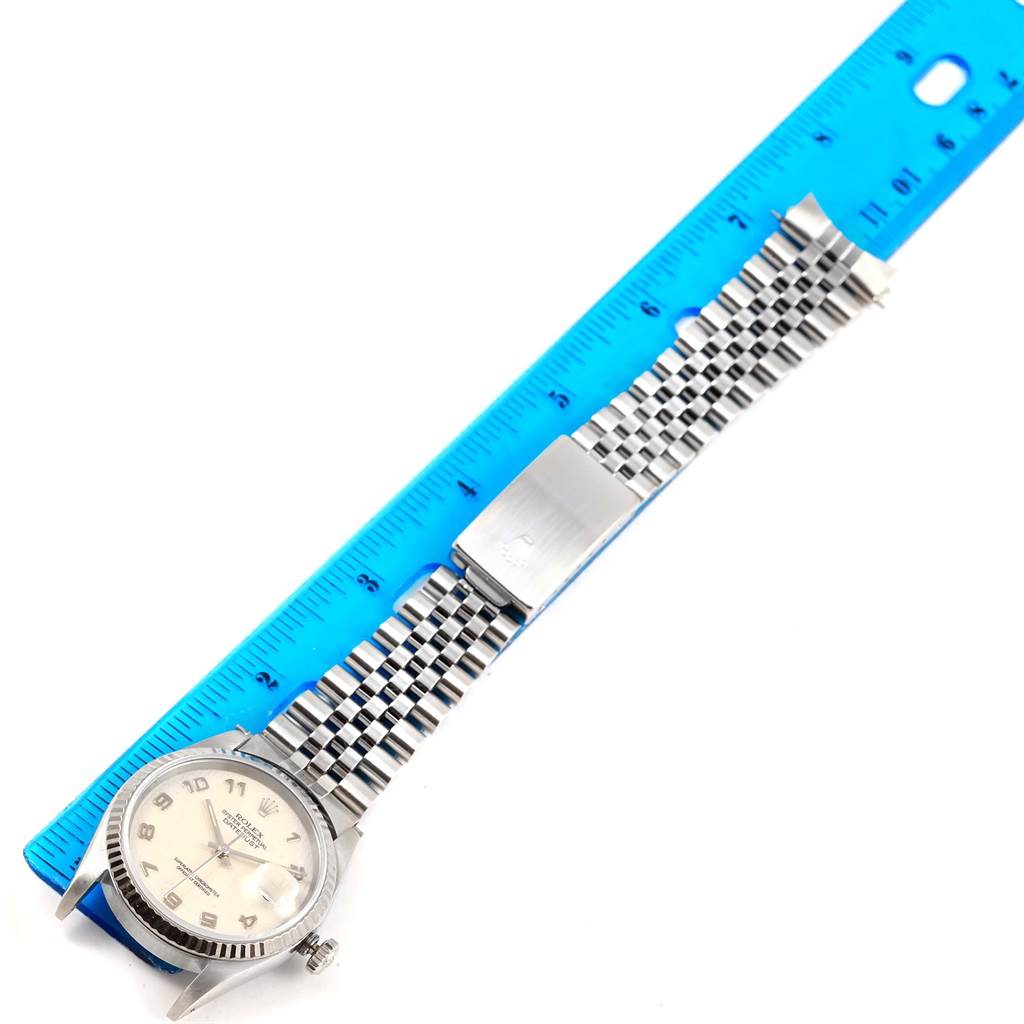 A Rolex Datejust 16234 Men's Stainless Steel Beige Dial 16234 Men's Stainless Steel Beige Dial watch is shown from an overhead angle, displaying the face, partially open Jubilee bracelet, and secured clasp with a ruler.