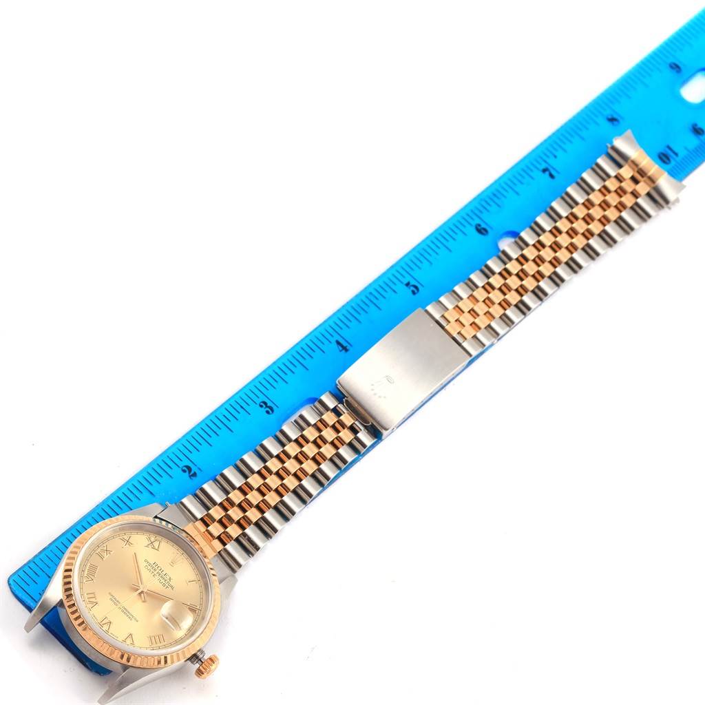 The image shows a top view of a Rolex Datejust 16233 Men's Steel and Gold (two tone) Champagne Dial 16233 Men's Steel and Gold (two tone) Champagne Dial watch with its face and metal bracelet band alongside a blue ruler.