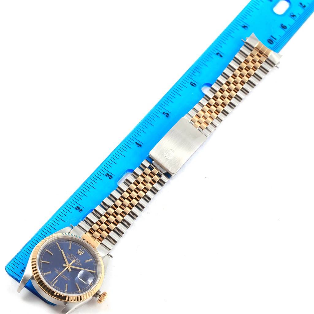 The image shows a top view of a Rolex Datejust 16233 Men's Steel and Gold (two tone) Blue Dial 16233 Men's Steel and Gold (two tone) Blue Dial watch with a blue dial and two-tone jubilee bracelet next to a ruler.