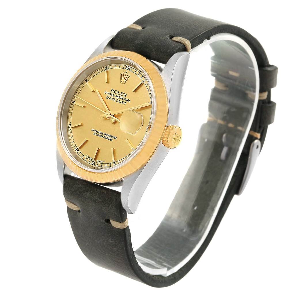 The Rolex Datejust 16233 Men's Steel and Gold (two tone) Champagne Dial 16233 Men's Steel and Gold (two tone) Champagne Dial watch is shown at a slight angle, highlighting its gold dial, fluted bezel, crown, and black leather strap.