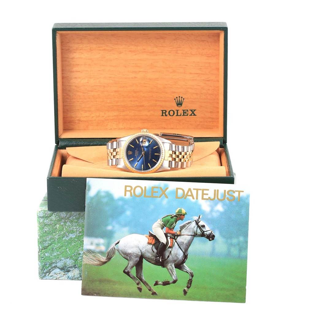 The Rolex Datejust 15223 Men's Steel and Gold (two tone) Blue Dial 15223 Men's Steel and Gold (two tone) Blue Dial watch is displayed head-on, in its open box with a booklet in the foreground.