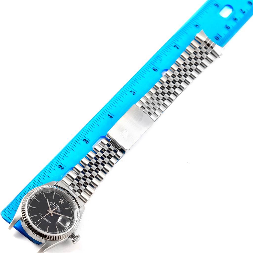 The Rolex Datejust 16234 Men's Stainless Steel Black Dial 16234 Men's Stainless Steel Black Dial watch is shown from a top angle, displaying the face, bezel, and bracelet alongside a blue ruler for scale.