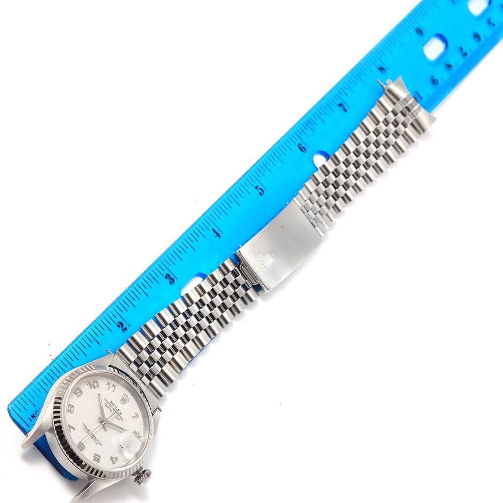 The Rolex Datejust 16234 Men's Stainless Steel Beige Dial 16234 Men's Stainless Steel Beige Dial watch is displayed at an angle with a focus on its bracelet and clasp next to a blue ruler.