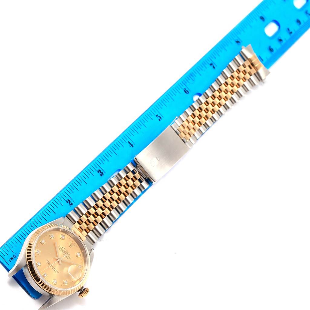 The image shows a Rolex Datejust 16233 Steel and Gold (two tone) Champagne Dial 16233 Steel and Gold (two tone) Champagne Dial watch placed horizontally with a blue ruler measuring its two-tone bracelet and face.