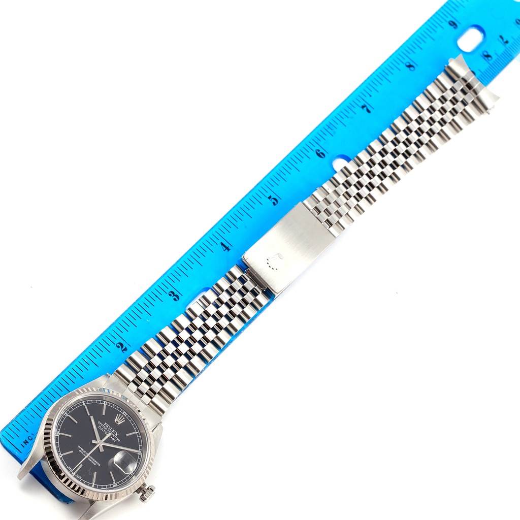 This is a top-down angle of a Rolex Datejust 16234 Men's Stainless Steel Black Dial 16234 Men's Stainless Steel Black Dial watch, displaying the face, bracelet, and part of the clasp alongside a blue ruler.