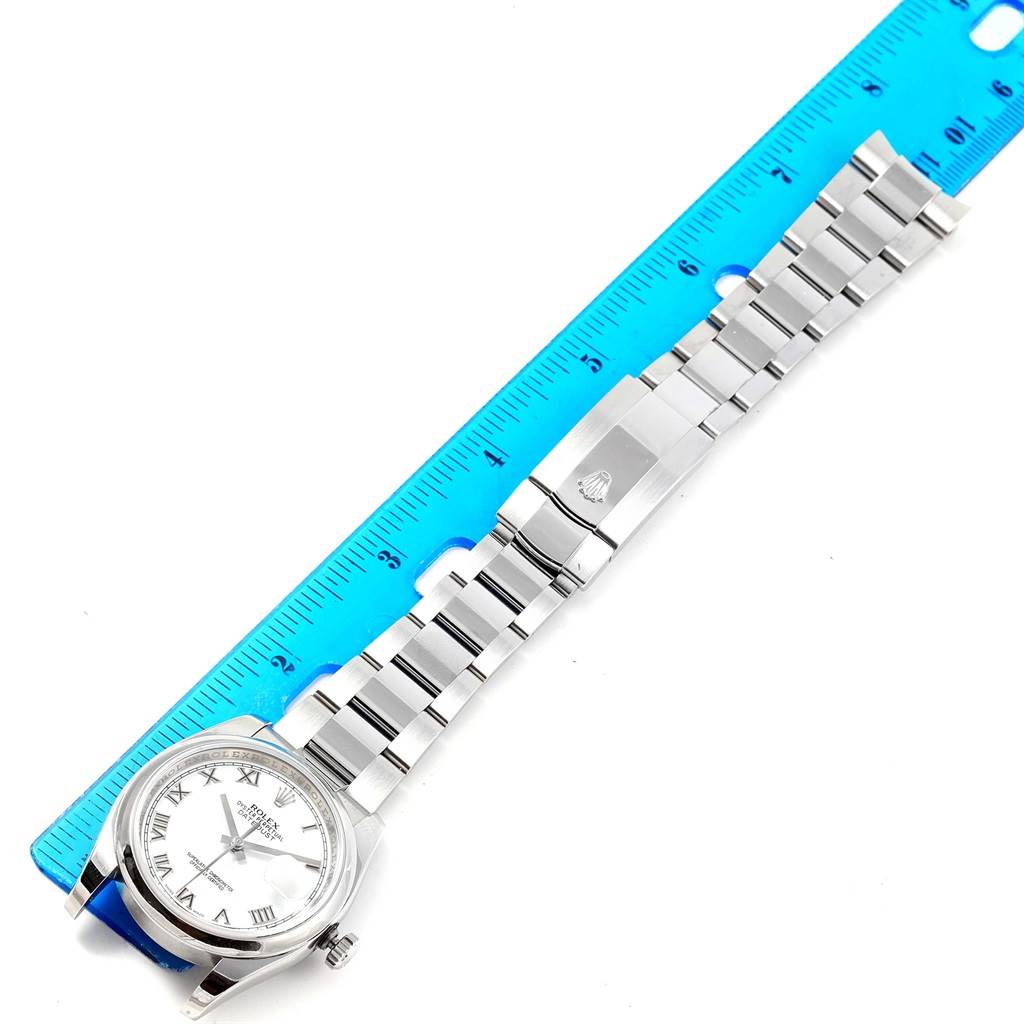 The Rolex Datejust 116200 Men's Stainless Steel White Dial 116200 Men's Stainless Steel White Dial watch is shown from a top-down angle alongside a measuring ruler, displaying its face and full metal bracelet.